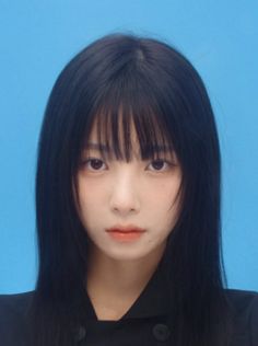 Woman with black hair and bangs wearing a black jacket against a blue background