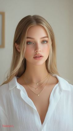 Woman with long blonde hair and green eyes wearing a white shirt and layered necklaces