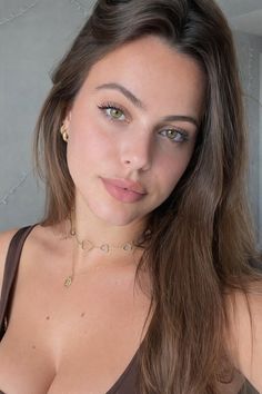 Woman with long brown hair and green eyes wearing a brown top and jewelry