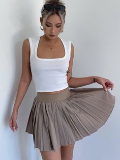 Woman with blonde hair and sunglasses on her head wearing a white crop top and pleated skirt