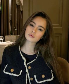 Woman with long brown hair wearing a black jacket with gold buttons in a restaurant
