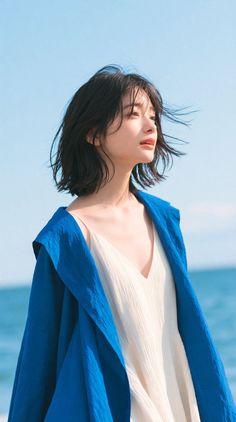 Woman with short hair and blue jacket over a white dress at the beach