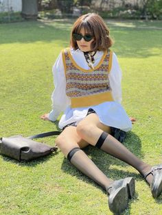 Woman with short hair and sunglasses sitting on grass in a sweater vest