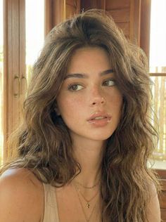 Woman with long wavy hair and freckles wearing layered necklaces indoors