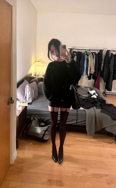 Woman in a black sweater, mini skirt, and stockings taking a mirror selfie