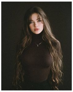 Woman with long hair and blue eyes wearing a dark turtleneck against a dark background