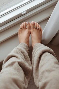 Bare feet with toe rings resting on a window sill, wearing sweatpants