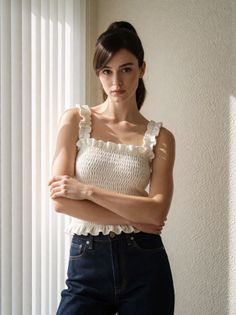 Woman in a white ruffled top and dark jeans with arms crossed indoors