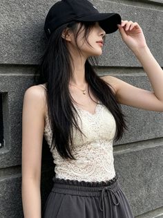 Woman in a black cap and lace top leaning against a gray wall