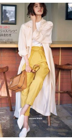 Woman with short hair wearing yellow pants and a long coat, holding a brown handbag