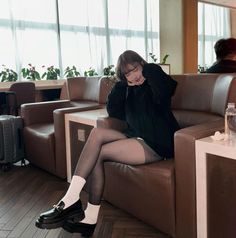 Woman in a black sweater and tights sitting on a brown couch indoors