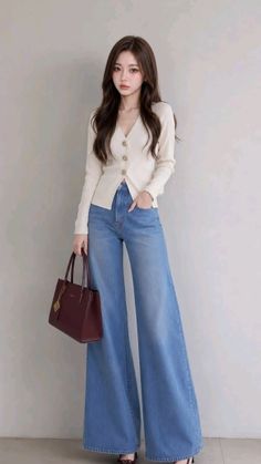 Woman with long brown hair wearing a cardigan and wide leg jeans, holding a handbag