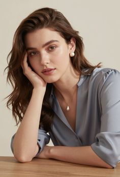 Woman with long brown hair wearing a blue shirt and pearl jewelry