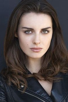 Woman with long brown hair and green eyes wearing a black leather jacket