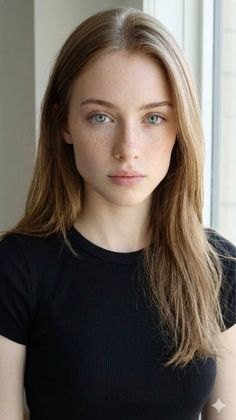 Young woman with long hair and freckles wearing a black t-shirt indoors