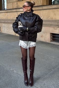 Woman in a leather jacket, white lace shorts, and knee-high boots on a street