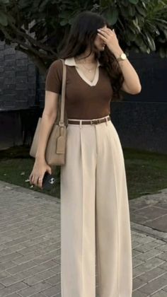 Woman in a brown top and wide leg pants holding a phone outdoors