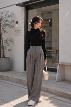 Woman in a black turtleneck and grey wide-leg pants standing outdoors