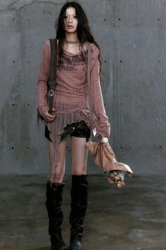 Woman with long black hair wearing leather shorts and black boots against a concrete wall