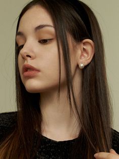 Young woman with long dark hair and pearl earrings looking down