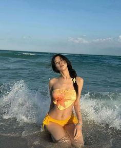 Woman in a yellow bikini kneeling in the ocean waves on a sunny day