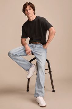 Man with curly hair wearing a black t-shirt and light wash jeans, sitting on a stool