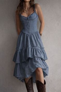 Woman in a blue corset dress and cowboy boots leaning against a wall