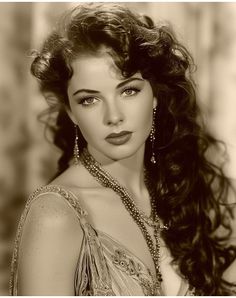 Woman with long curly hair and ornate jewelry in a sepia-toned portrait