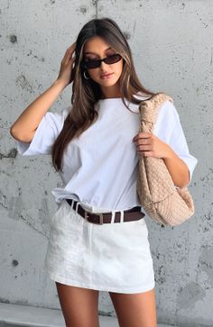 Woman in a white t-shirt and skirt with a woven bag against a concrete wall
