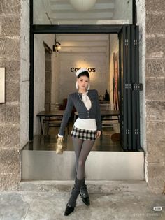 Woman in a plaid skirt, cropped cardigan, and leg warmers standing indoors