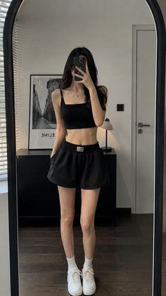 Woman in a black crop top and shorts taking a mirror selfie