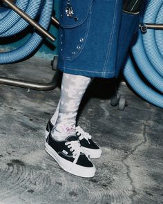 Person wearing denim shorts, patterned socks, and black sneakers on a concrete floor