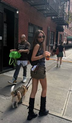 Woman in a mini skirt and tall boots walking a dog on a city street