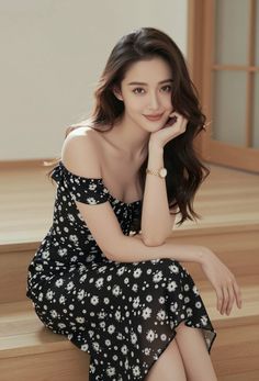 Woman in a black off-shoulder floral dress sitting indoors