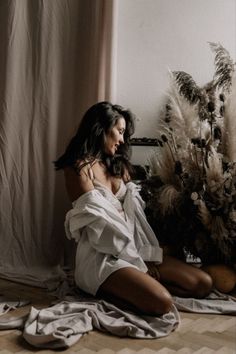 Woman in a white shirt and lace bra kneeling on the floor with dried plants