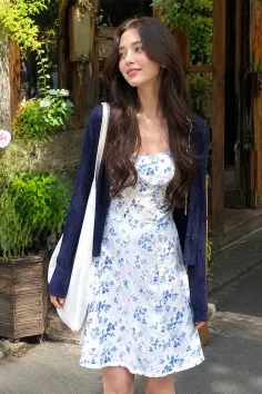 Woman in a white floral dress and blue cardigan outdoors