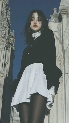 Woman with black hair and red lipstick wearing a black top and white skirt outdoors