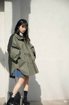 Woman with long black hair wearing a green coat and blue skirt outdoors