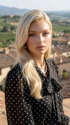 Woman with blonde hair wearing a polka dot blouse and pearl necklace outdoors