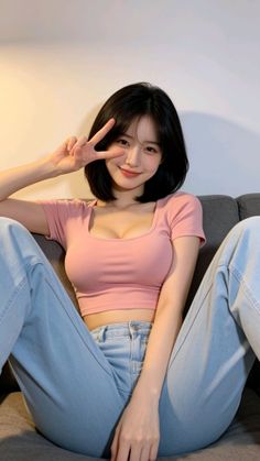 Woman with short black hair in a pink crop top and jeans making a peace sign