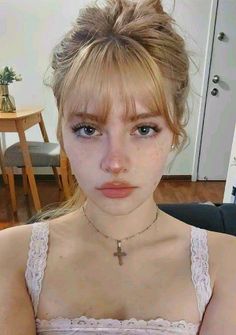 Young woman with blonde hair and bangs wearing a lace top and cross necklace