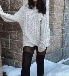 Person in a cable knit sweater and black tights standing outdoors near a brick wall