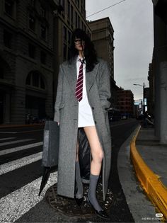 Person in a long coat, white shirt, and tie on a city street