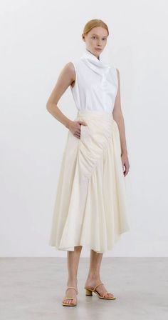 Woman with red hair wearing a white sleeveless shirt and cream skirt