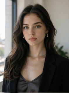 Woman with long dark hair and green eyes wearing a black blazer and gold jewelry