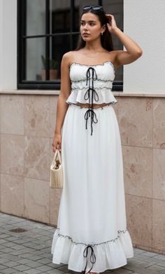 Woman in a white two-piece outfit with a straw bag standing outdoors