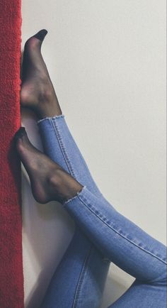 Legs in blue jeans and sheer socks resting against a wall