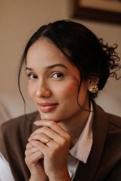 Woman with dark hair wearing gold earrings and a brown vest