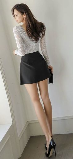 Woman in a white lace top and black mini skirt with high heels posing indoors