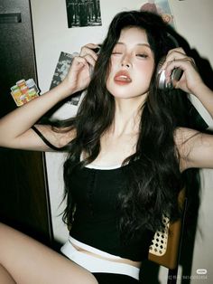 Woman with long dark hair wearing headphones and a black top, sticking out her tongue